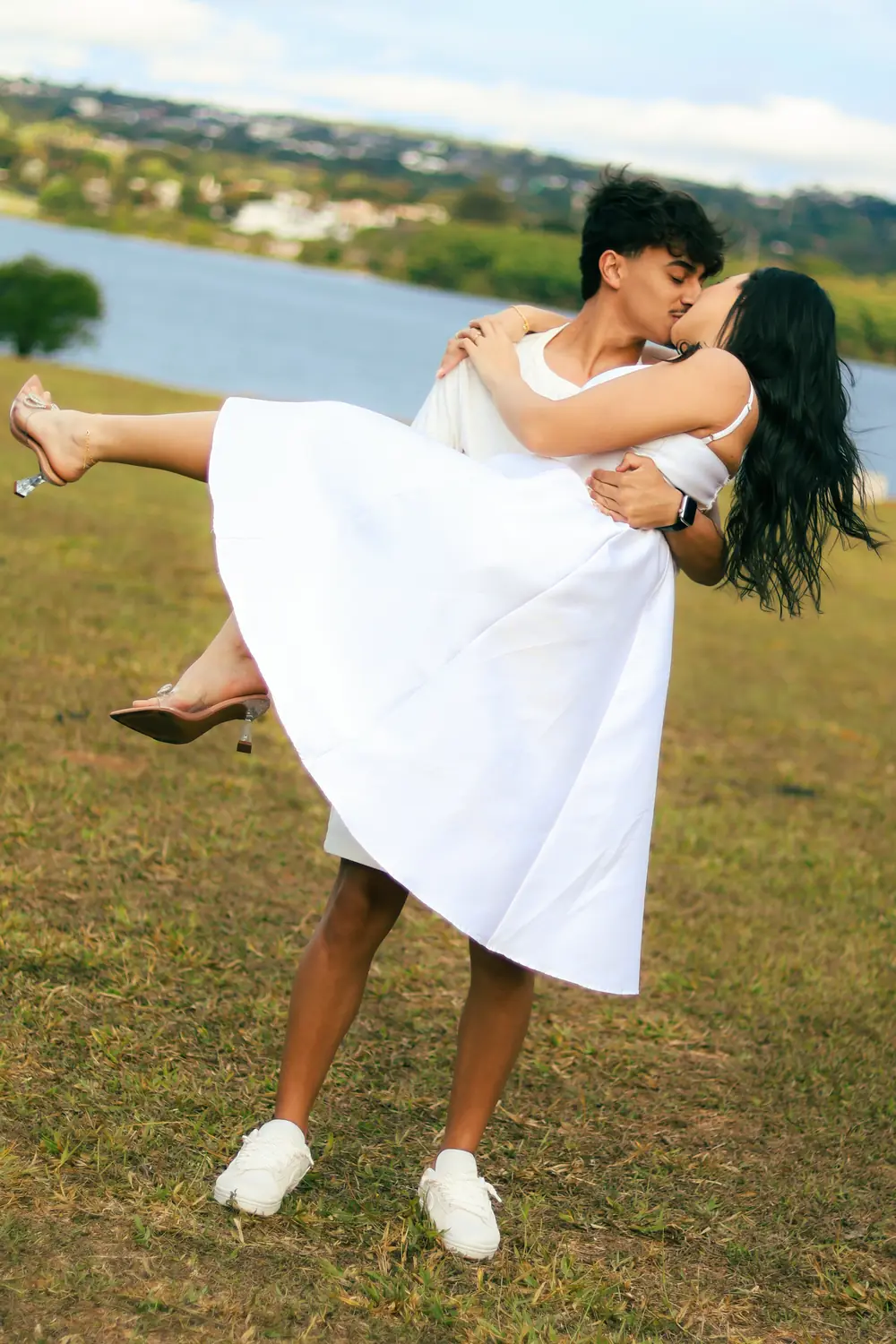 Casal num gramado à beira do lago, ele levantando ela no colo