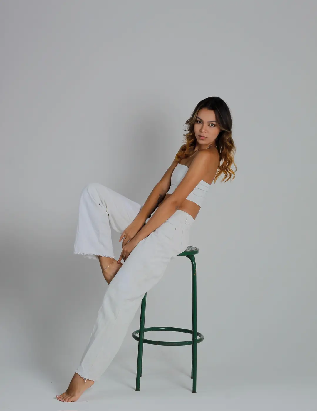 Modelo de calça branca sentada num banco de estúdio