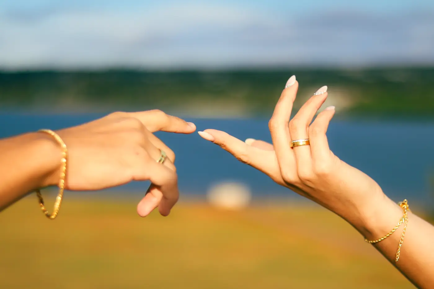Mãos de um casal com alianças diante de um lago